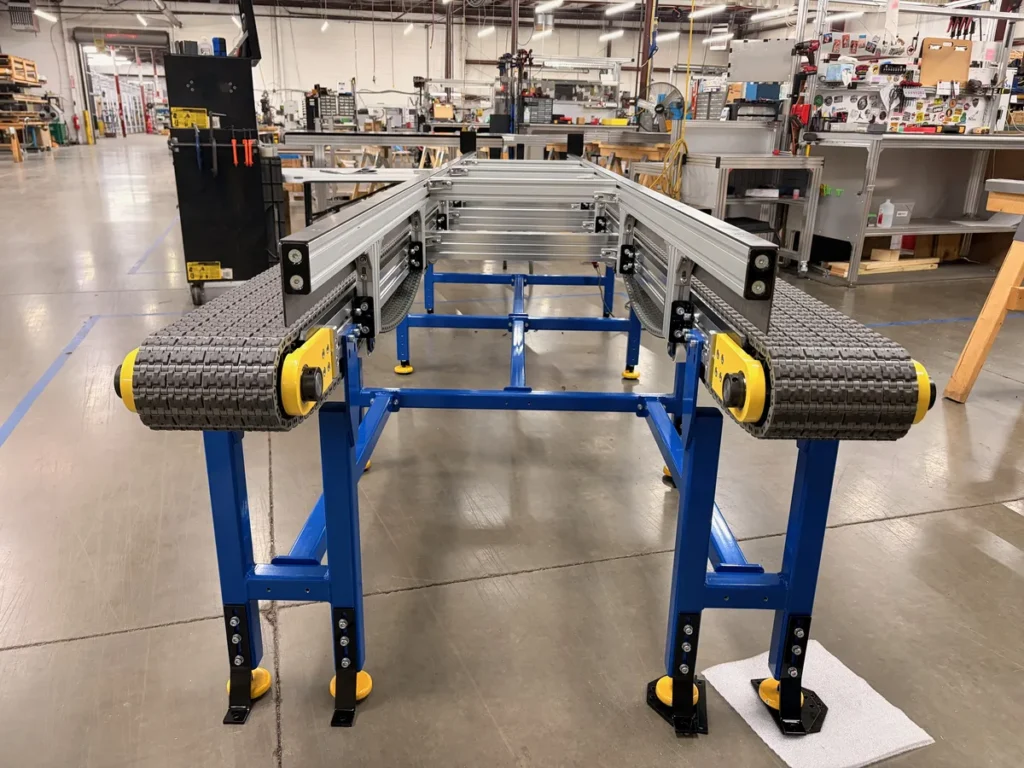 Dual lane modular plastic belt conveyor for heavy parts, end view showing both belt lanes and blue tubular steel frame